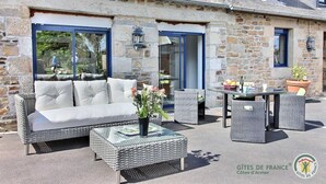 Un bâtiment en pierre doté d’un espace extérieur aménagé avec des canapés et des tables, et d’une enseigne indiquant « Gîtes de France ».