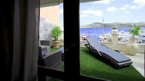 Ein Balkon mit Liegestuhl und Topfpflanze mit Blick auf einen Yachthafen und eine Bergkulisse.