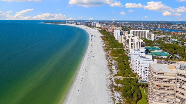 Un paisaje urbano costero con una extensa playa de arena, edificios altos y un cielo azul despejado.