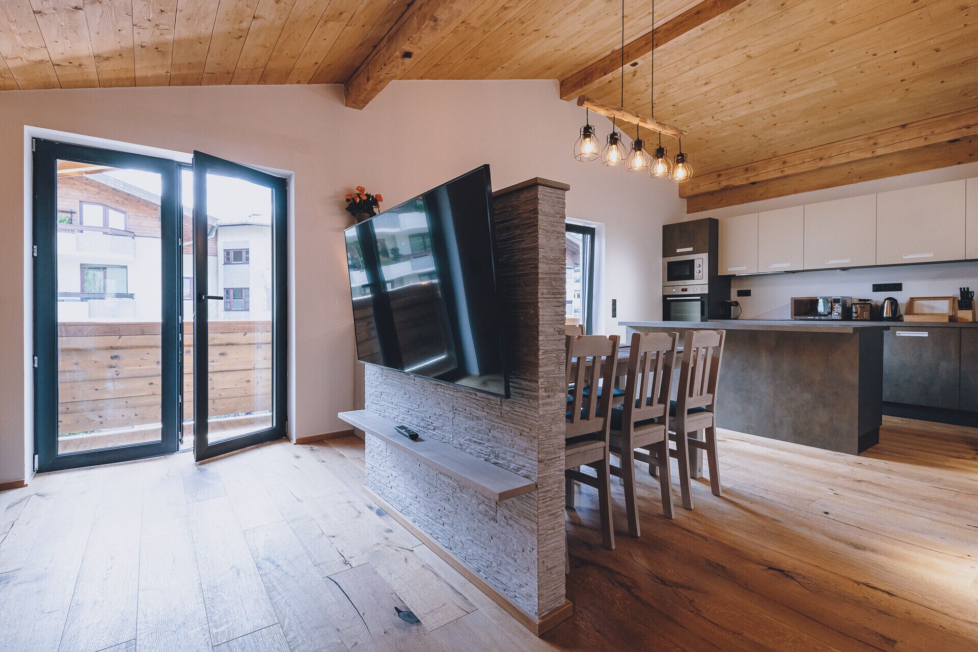 Eine moderne Küche mit integriertem Fernseher, Holzboden und einem Essbereich mit Stühlen.