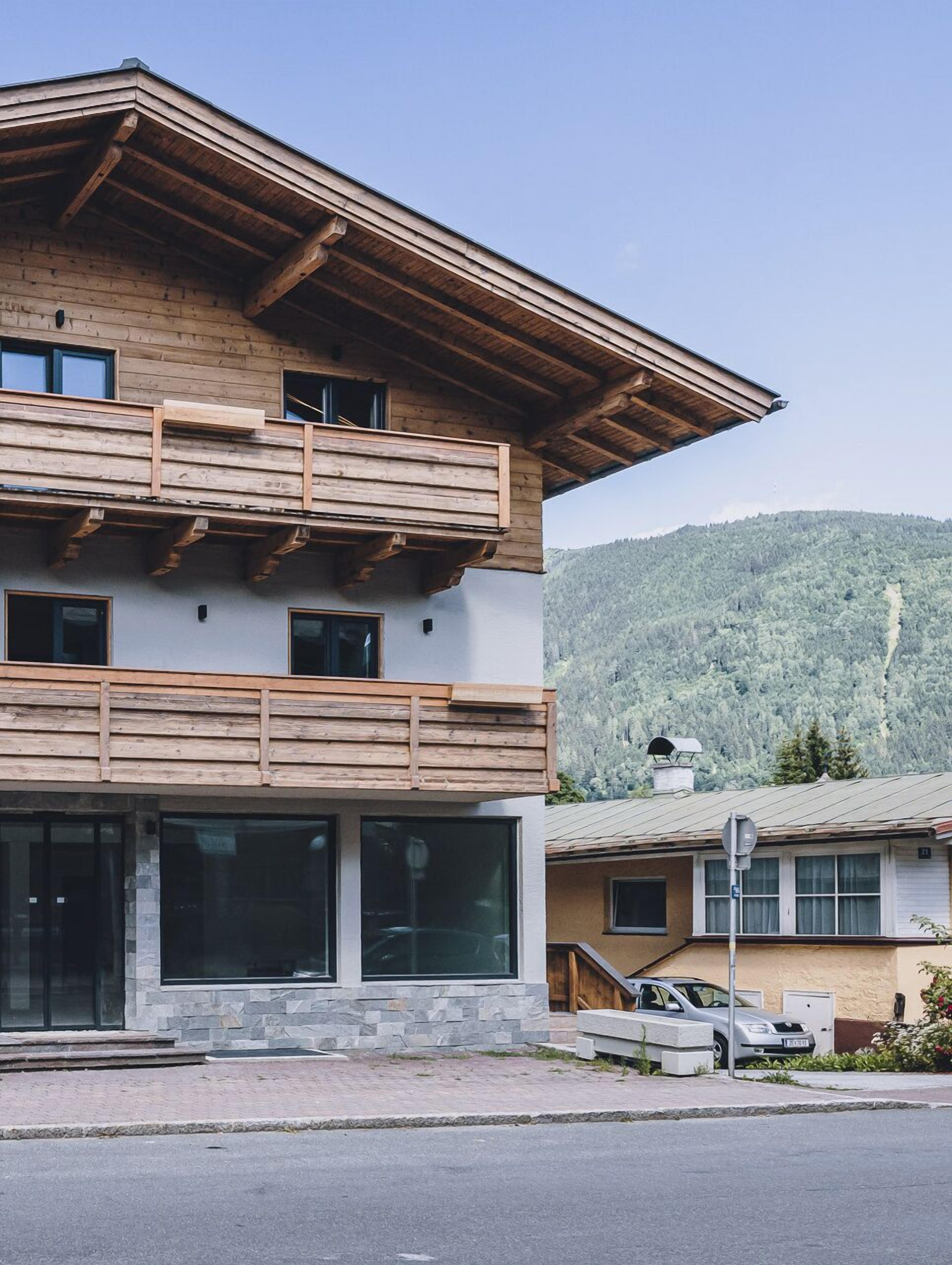 Ein zweistöckiges Gebäude mit einem hölzernen Balkon und großen Fenstern, vor einer Berglandschaft gelegen.