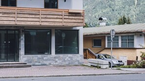 Un edificio de dos pisos con balcón de madera y ventanas amplias, con montañas al fondo.