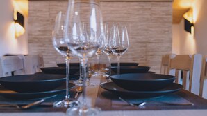 Una mesa de comedor preparada con varias copas de vino y platos, con una pared de madera y luces fijadas a la pared al fondo.