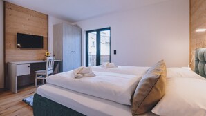 Une chambre d’hôtel moderne avec un grand lit, un bureau et un téléviseur fixé au mur.