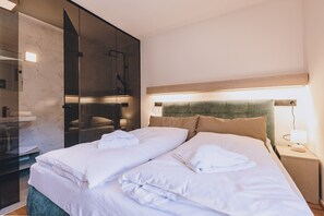 Ein modernes Hotelzimmer mit einem großen Bett, einer Duschkabine aus Glas und einem hölzernen Kopfteil.