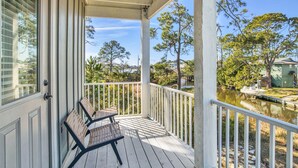 A covered porch with two wicker chairs, a white railing, and a view of a lake with a boat.