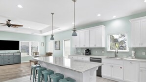 A modern kitchen with a large island, bar stools, white cabinets, and pendant lighting.