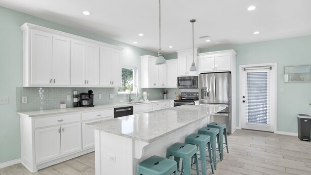 A modern kitchen with white cabinets, a large island with bar stools, stainless steel appliances, and pendant lighting.
