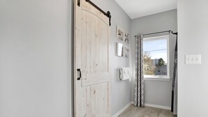 A hallway with a wooden door, a window with curtains, and a wall with framed pictures.