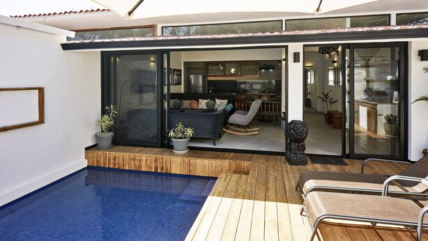 A modern outdoor living area with a pool, wooden deck, and a seating area with a sofa and chairs. - Villa Taleona (Cóbano)