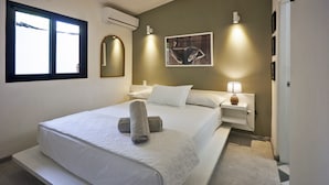 A neatly made bed with white linens and rolled towels, a bedside table with a lamp, a wall-mounted mirror, and a framed picture. - Villa Taleona (Cóbano)
