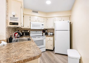 A compact kitchen with a granite countertop, white appliances, and a trash bin. - 3648 Orlando Vacational Apartment 2nd floor, Lake view (Orlando)