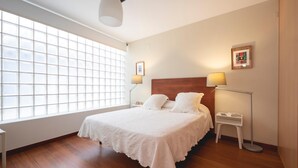 A bedroom with a large window, a wooden headboard, a white bed, two bedside tables, and a floor lamp. - Bravissimo Casa Magnolia, one-bedroom apartment near Girona’s ancient wall (Girona)