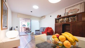 A modern living room with a glass dining table, a sofa, and a coffee table. There is a wooden cabinet with decorative items and a framed map on the wall. - Bravissimo Casa Magnolia, one-bedroom apartment near Girona’s ancient wall (Girona)