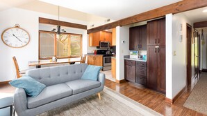 A modern kitchen with wooden cabinets, a microwave, and a dining area with a grey sofa and wooden table.