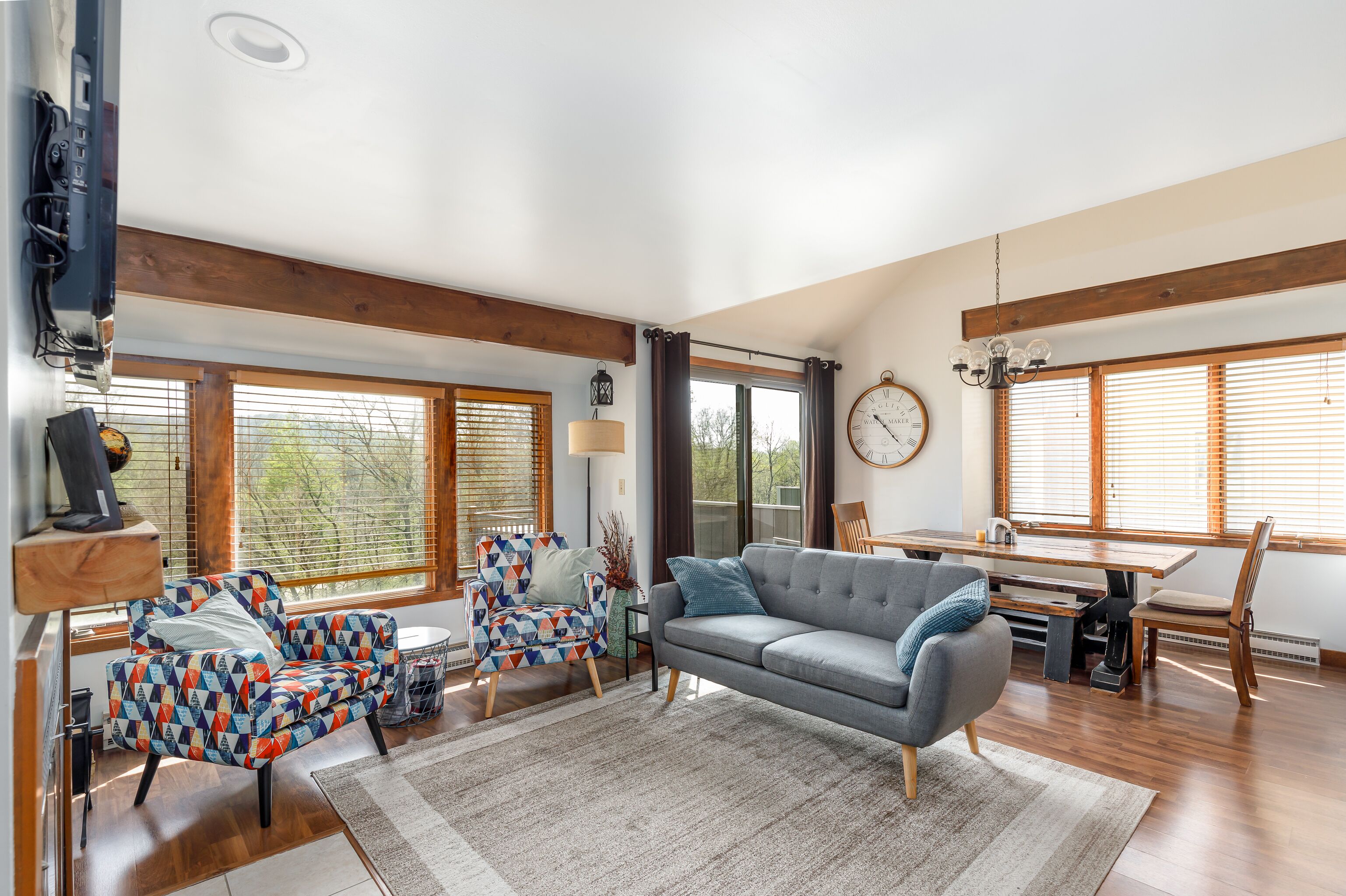 A spacious living room with a grey sofa, colorful armchair, and a dining area with wooden furniture.