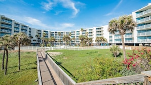 A hotel with multiple balconies, a grassy area, and palm trees. - Sandcastle Condominium Unit 111 (Port Aransas)