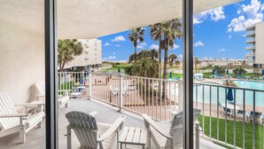 Un balcon avec des fauteuils Adirondack blancs, une piscine et des palmiers.