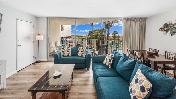 Un salon moderne comprenant un ensemble de canapés, une table à manger et donnant sur un balcon aménagé avec du mobilier d’extérieur.