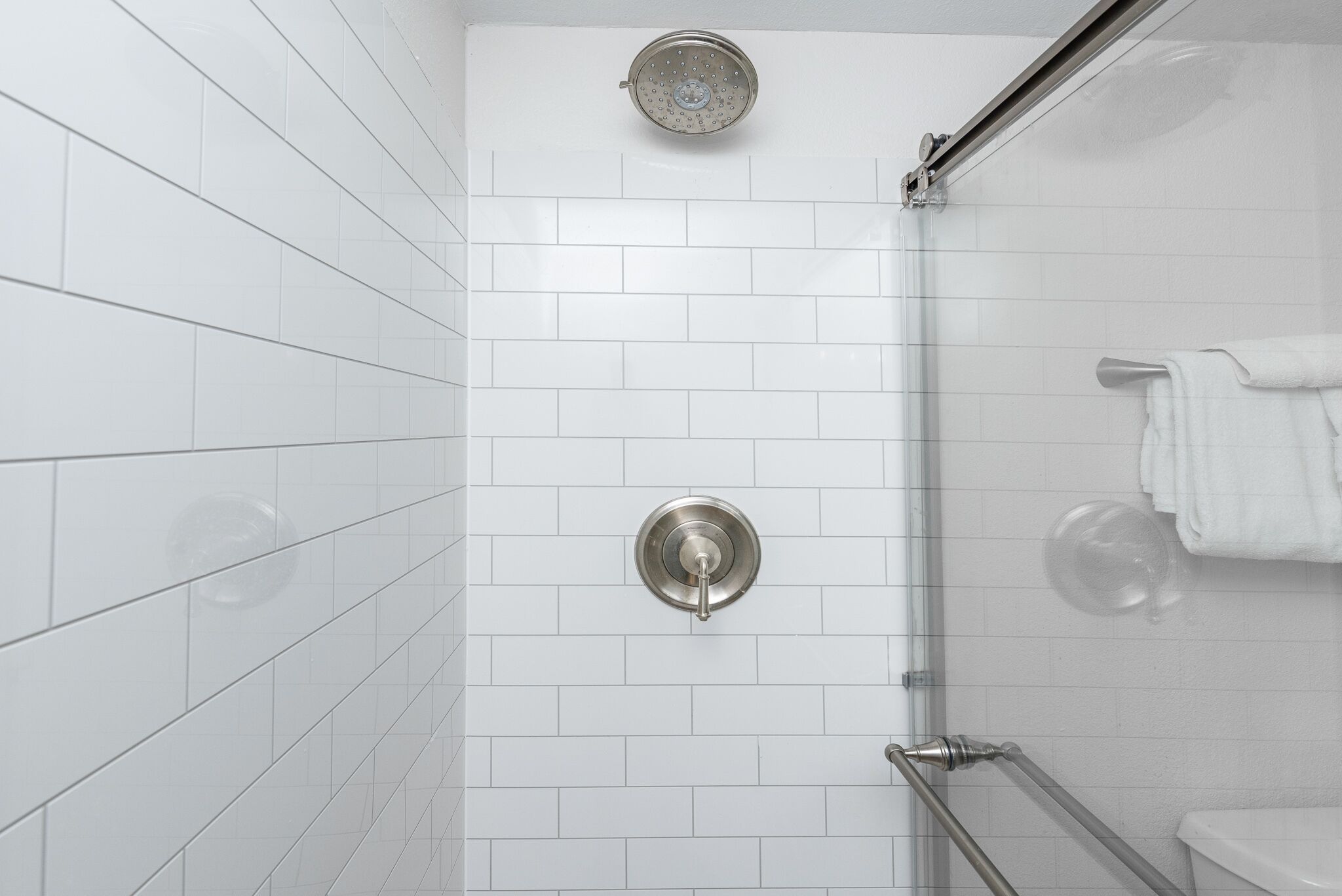 Een moderne badkamer met witte metro tegels, een glazen douchecabine en een toilet met een handdoekhouder.