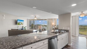 A modern kitchen with granite countertops, stainless steel appliances, and a large window overlooking a balcony. - Sandcastle Condominium Unit 137 (Port Aransas)
