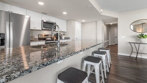 A modern kitchen with a granite countertop, stainless steel appliances, and a central island with bar stools. - Sandcastle Condominium Unit 137 (Port Aransas)