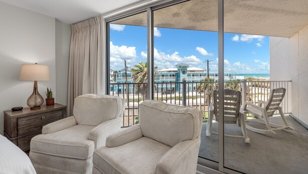 A balcony with two rocking chairs, a small table, and a lamp. - Sandcastle Condominium Unit 214 (Port Aransas)