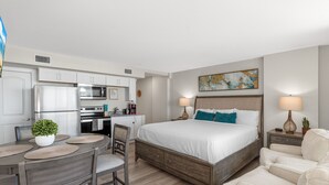 A hotel room with a bed, bedside tables, a desk with a chair, a kitchenette, and a dining area. - Sandcastle Condominium Unit 214 (Port Aransas)