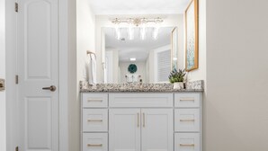 A bathroom with a white vanity, a large mirror, and a light fixture above the mirror. - Sandcastle Condominium Unit 214 (Port Aransas)