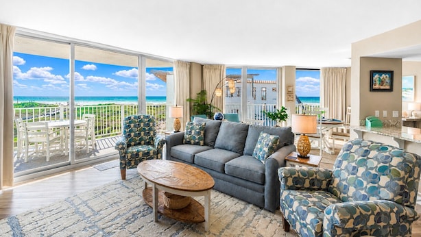 A spacious living room with a balcony overlooking the ocean, a grey sofa, patterned armchairs, and a coffee table. - Sandcastle Condominium Unit 237 (Port Aransas)