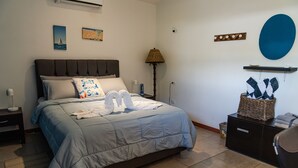 A bedroom with a large bed, a nightstand, a lamp, a wall-mounted shelf, and a trash bin. - Beachfront One Bedroom on Tamarindo Beach (Tamarindo)