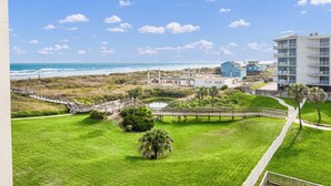 A coastal hotel with a view of the ocean, a bridge, and a well-maintained lawn. - Sandcastle Condominium Unit 311 (Port Aransas)