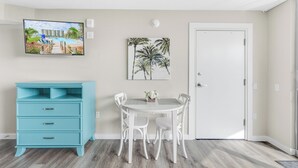 A room with a white door, a blue dresser, a dining table with four chairs, and a painting of palm trees on the wall. - Sandcastle Condominium Unit 311 (Port Aransas)