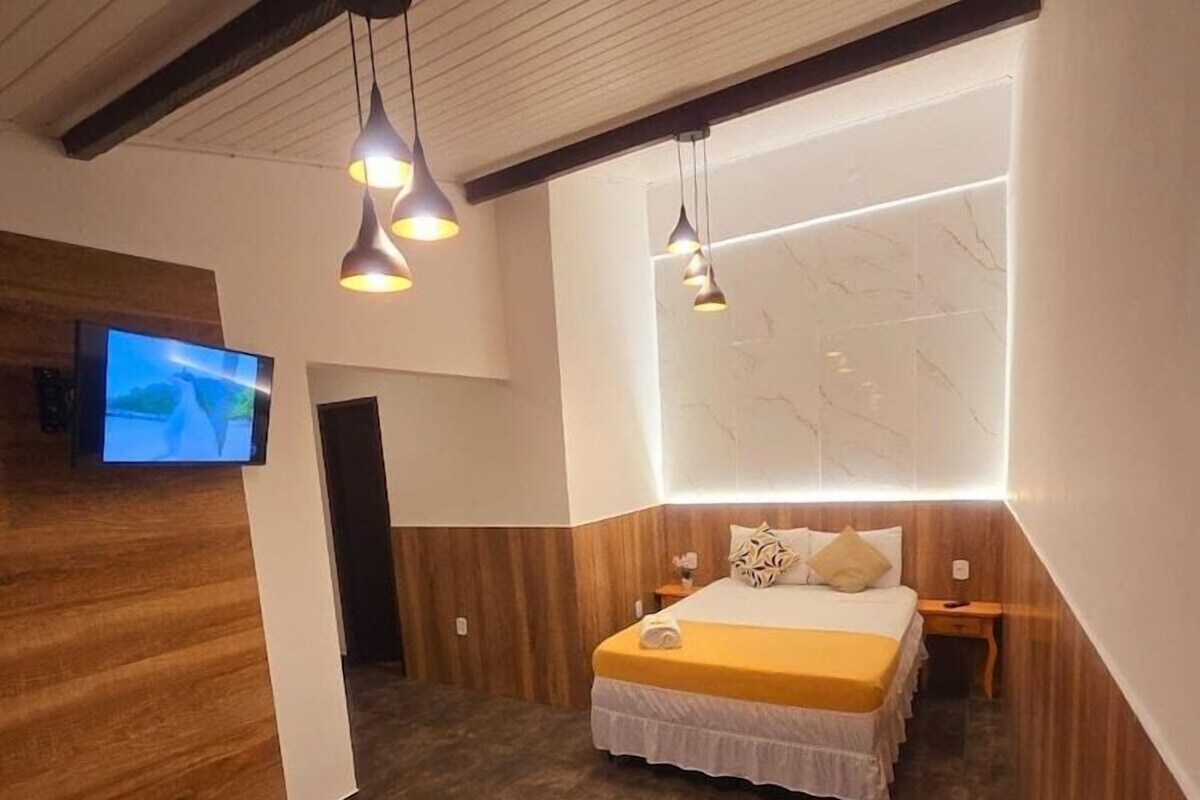 A modern hotel room with a bed, bedside tables, a TV, and a yellow sofa.