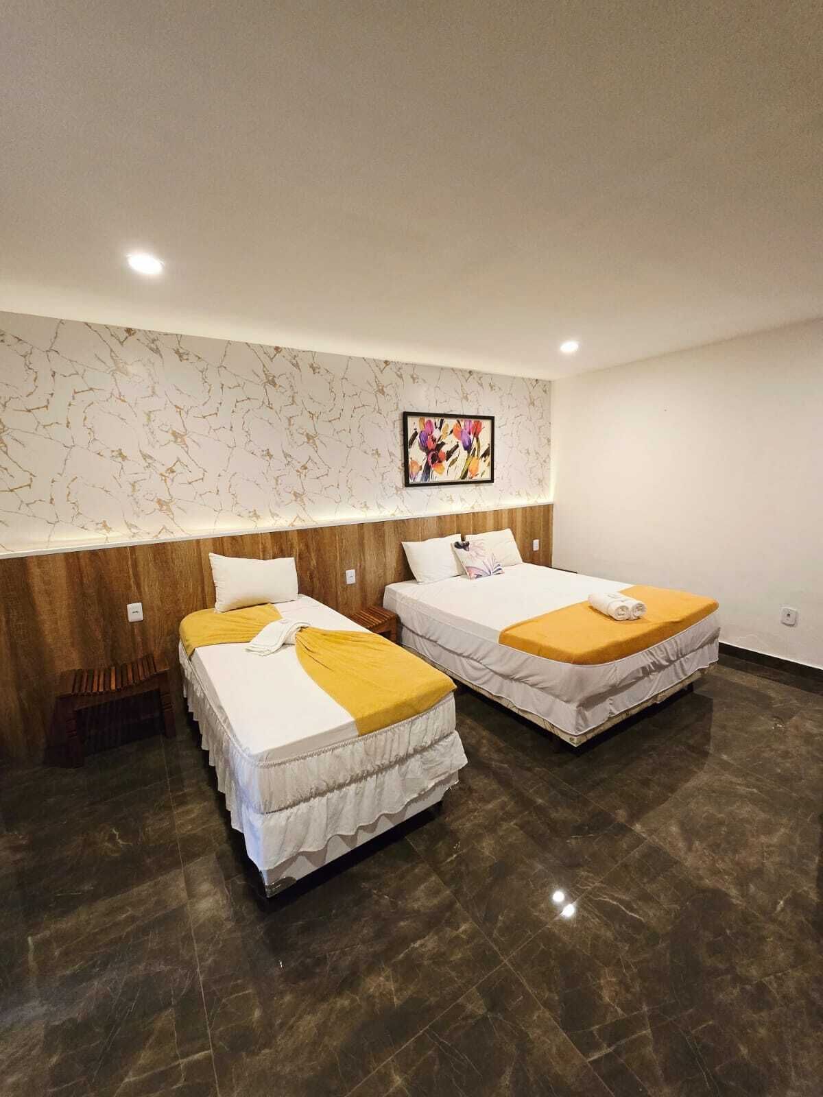 A hotel room with two beds, a marble-patterned wall, and a framed floral artwork.