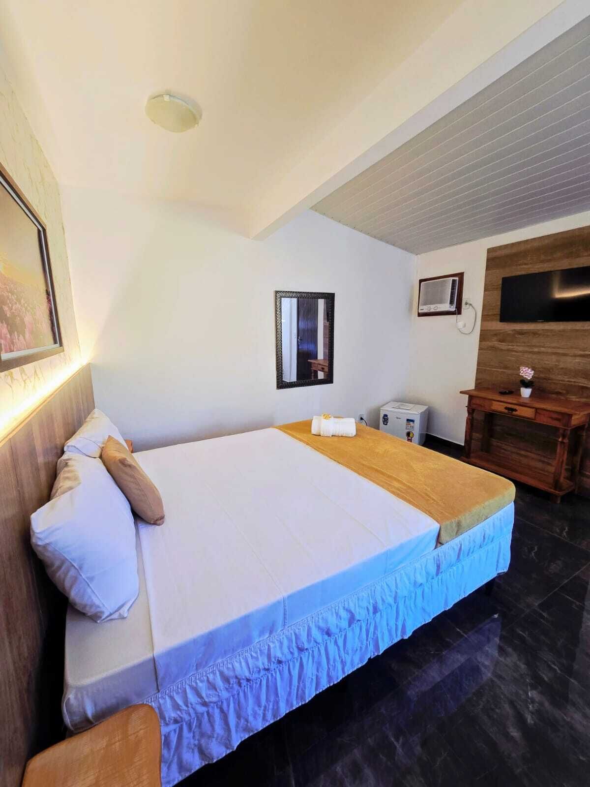 Un dormitorio con una cama, una mesita de noche, un espejo, un televisor y un calentador fijado a la pared.