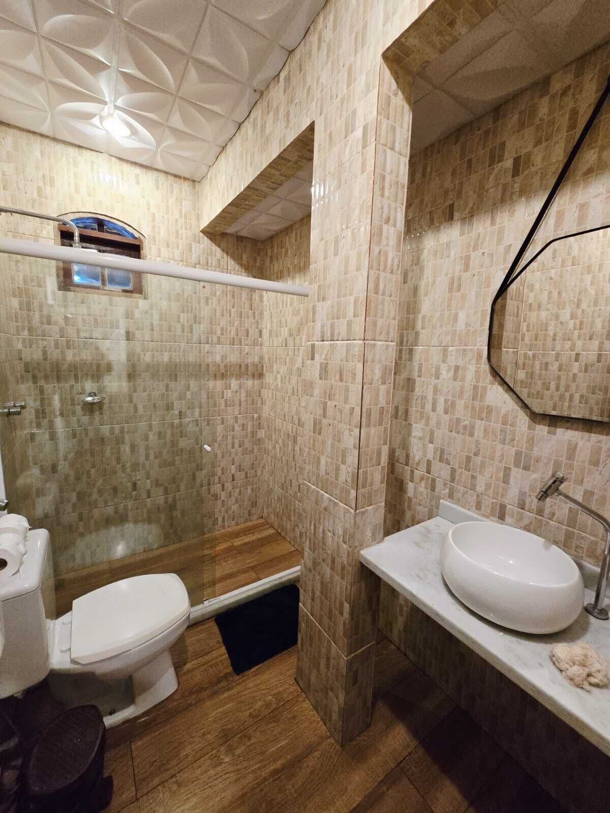A bathroom with a shower, toilet, and sink, featuring tiled walls and wooden flooring.