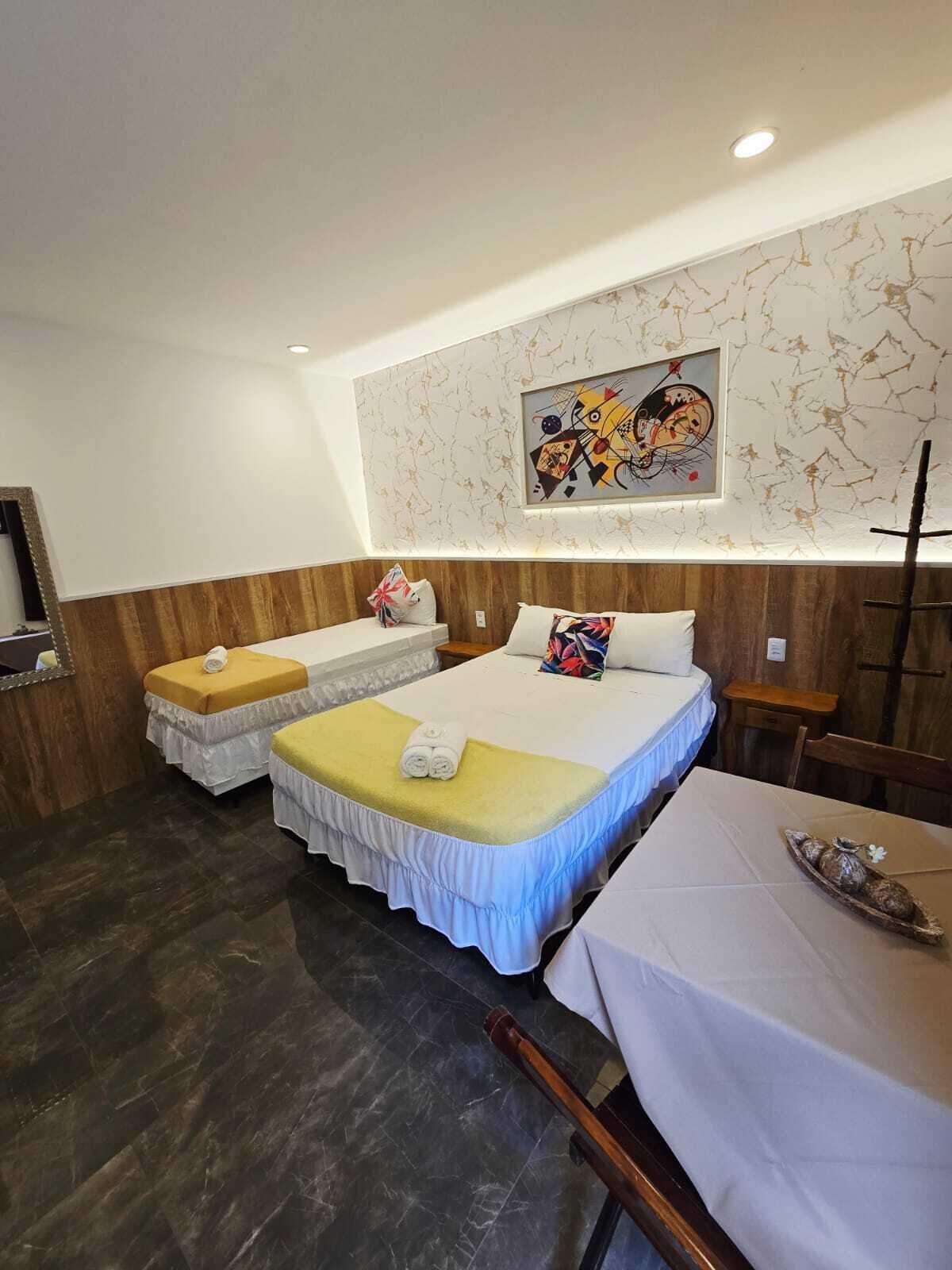 A hotel room with a bed, a small table, a chair, and a painting on the wall.