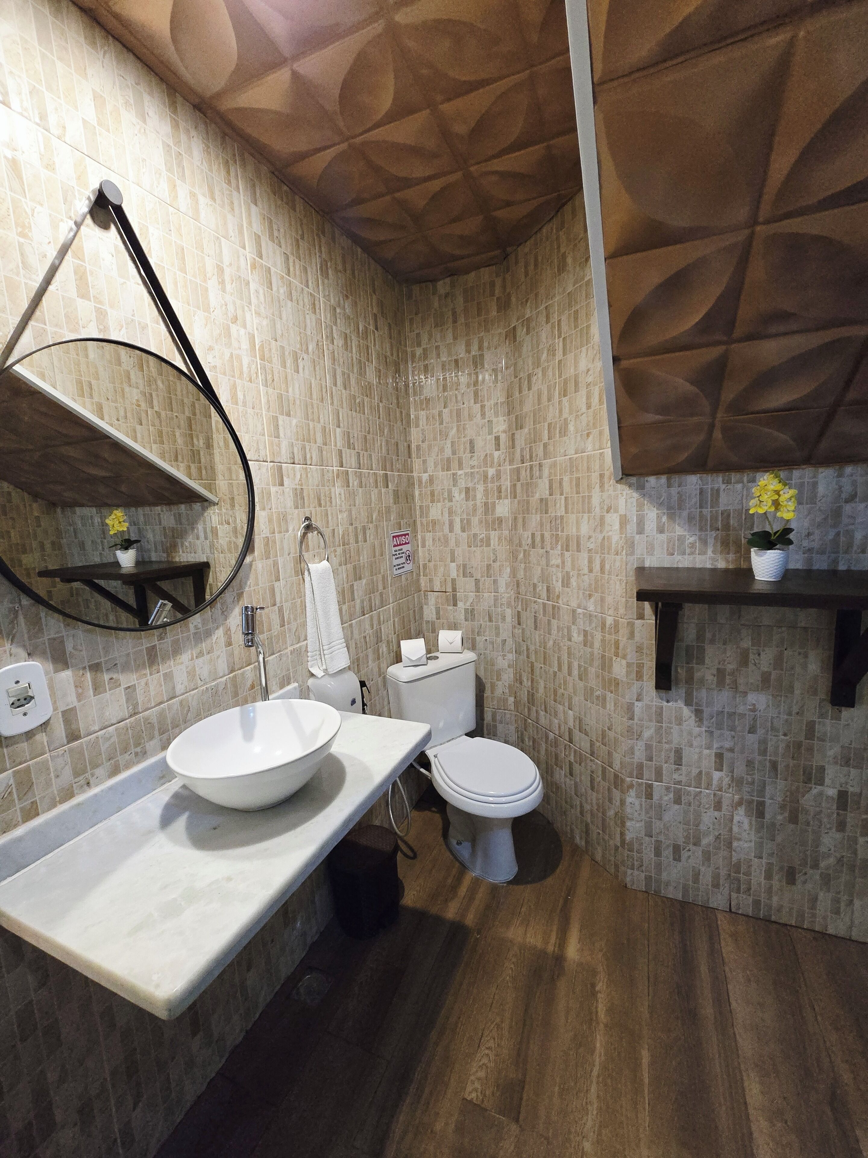 A bathroom with a white sink, toilet, and mirror, tiled walls, and wooden flooring.