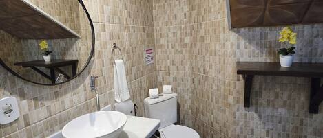 A bathroom with a white sink, toilet, and mirror, tiled walls, and wooden flooring.