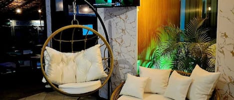 A modern living area with a hanging chair, a round sofa, a flat-screen TV, and a wall-mounted light fixture.