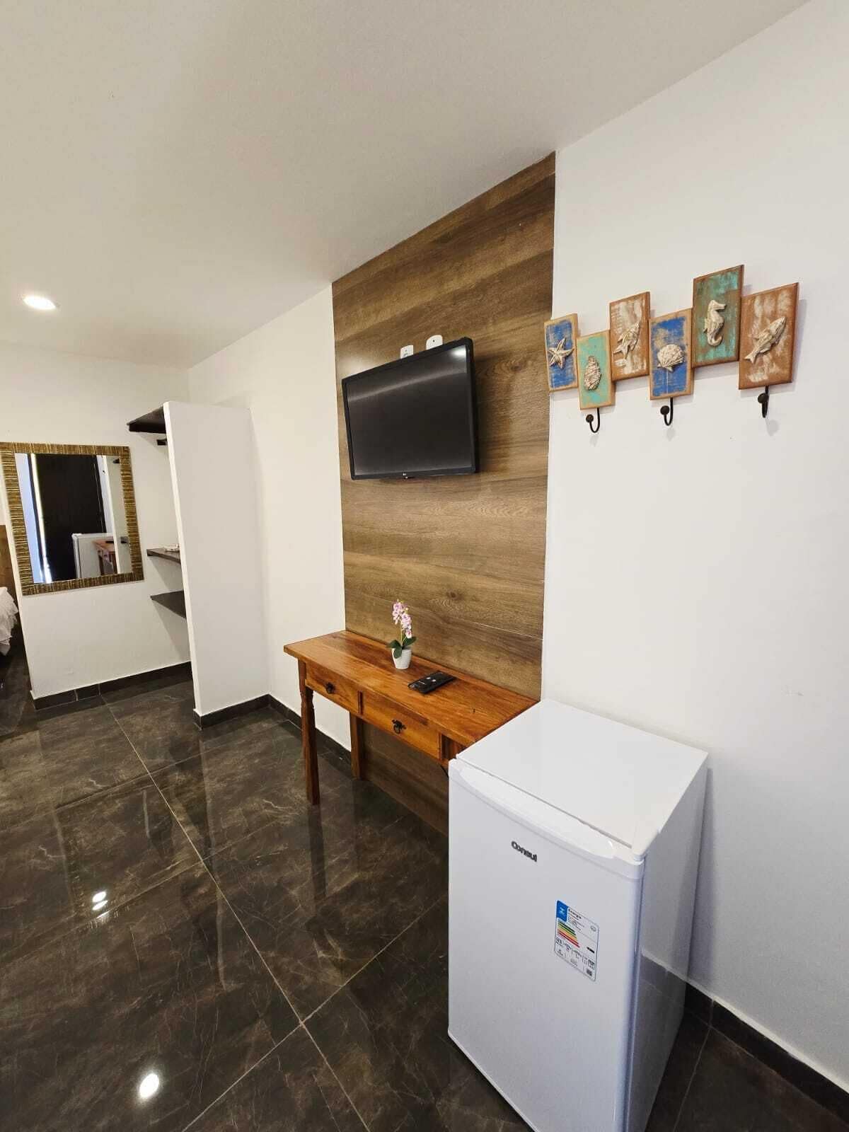 A modern kitchen with a flat-screen TV, a wooden wall panel, a small table with a vase, and a refrigerator.