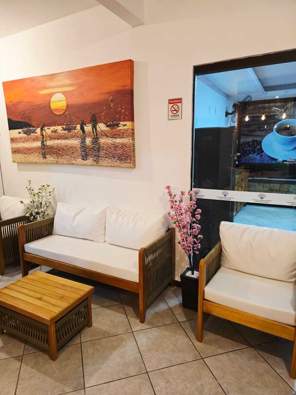 A room with a sofa, two wooden chairs, a wooden coffee table, a painting of a sunset scene, and a window with a view of a pool.
