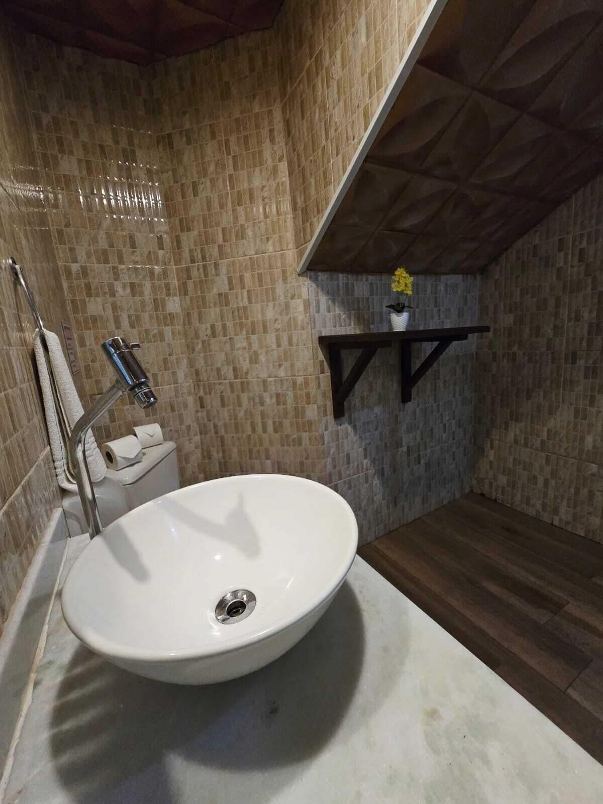 A bathroom with a white sink, a towel rack, a toilet, and a shelf with a flower.