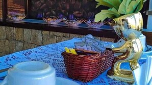 Una mesa con mantel azul, una tetera blanca, una taza, una cesta con dinero y flores amarillas.