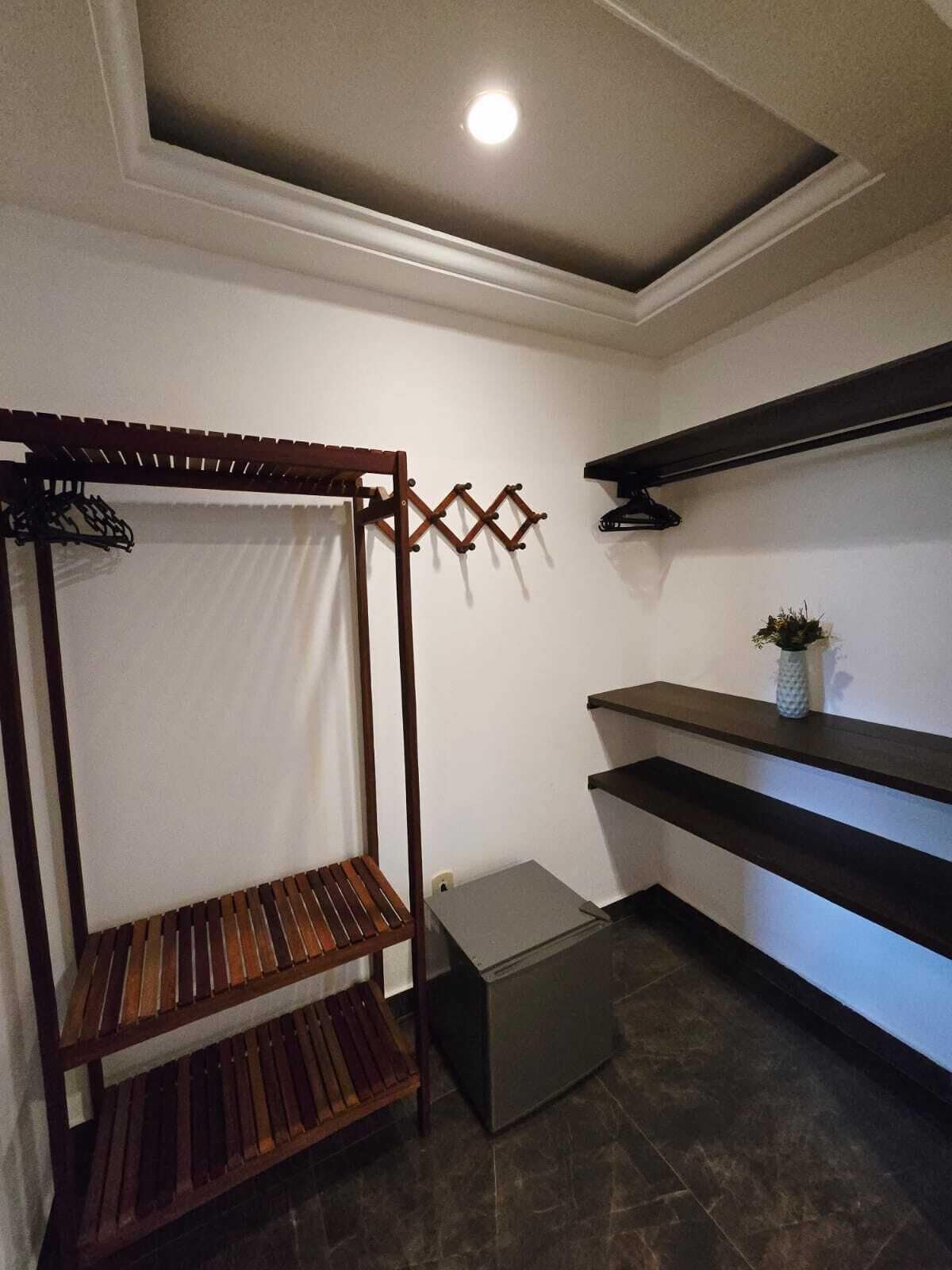 Une pièce avec un banc en bois, des étagères fixées au mur, une petite plante en pot et un spot encastré au plafond.
