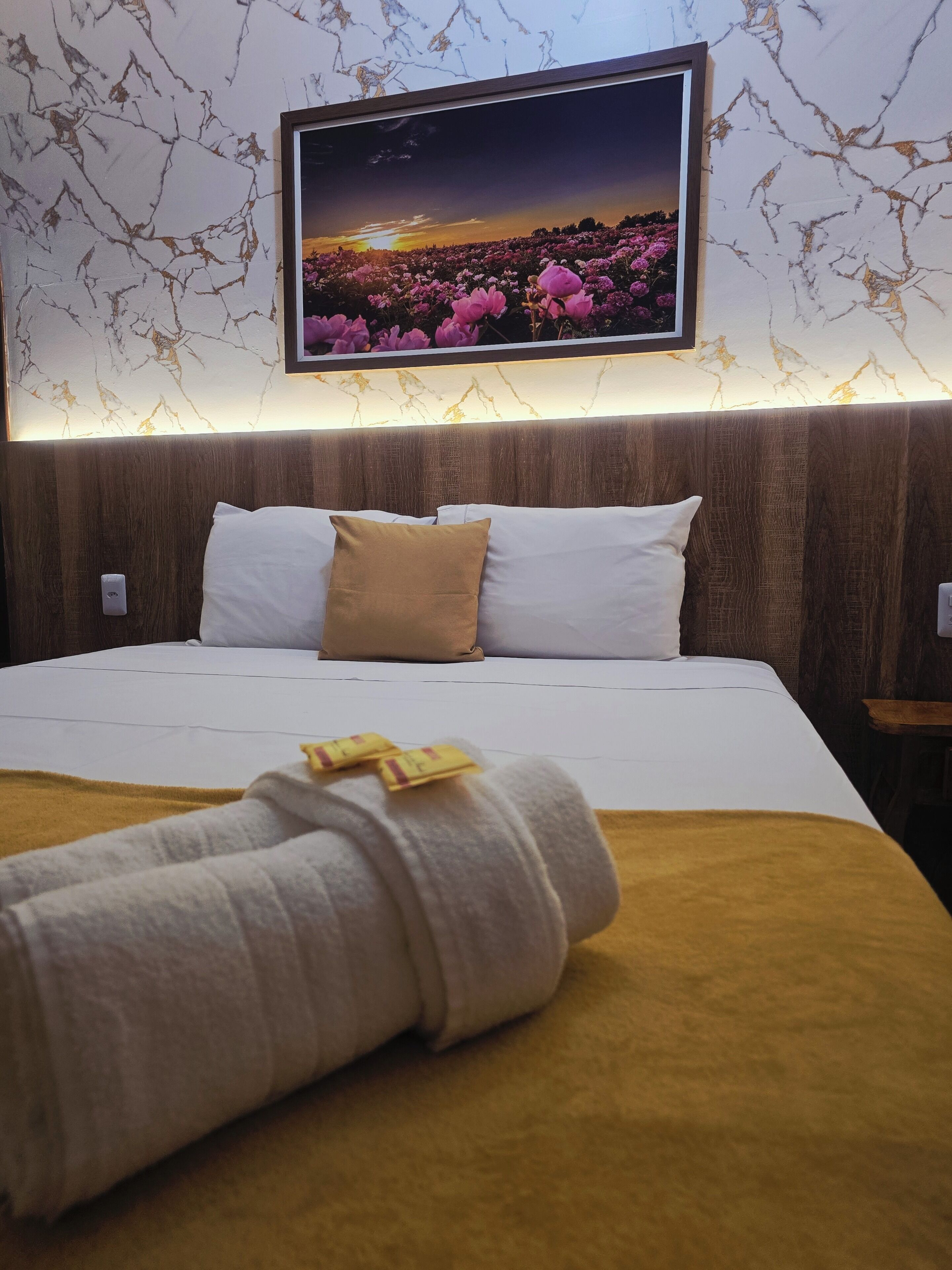 Een hotelkamer met een bed, kussens, een deken, een tv aan de muur en een houten hoofdeinde.