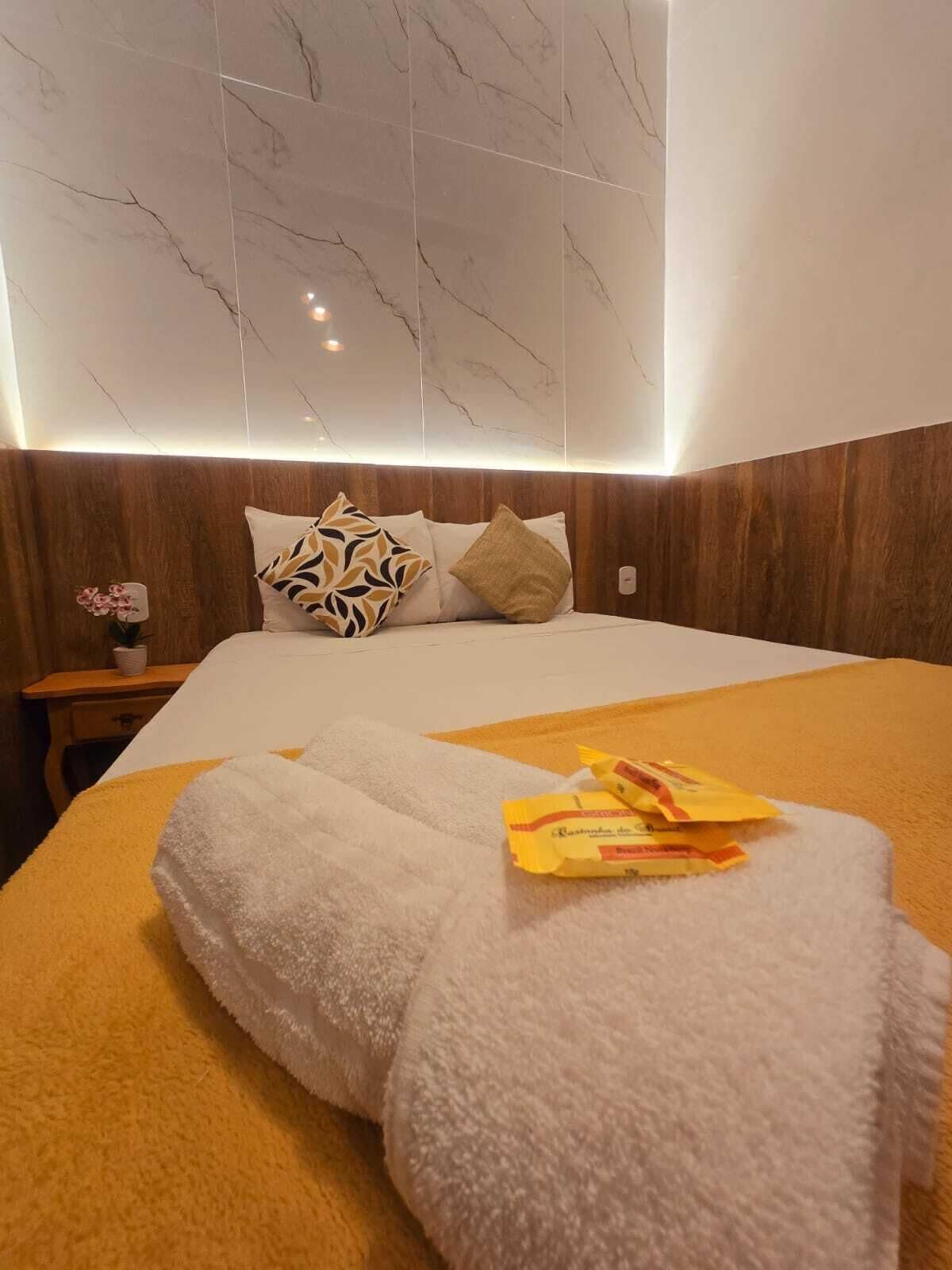 A hotel room with a marble-patterned ceiling, a bed with multiple pillows, a nightstand with a plant, and a towel on the bed.