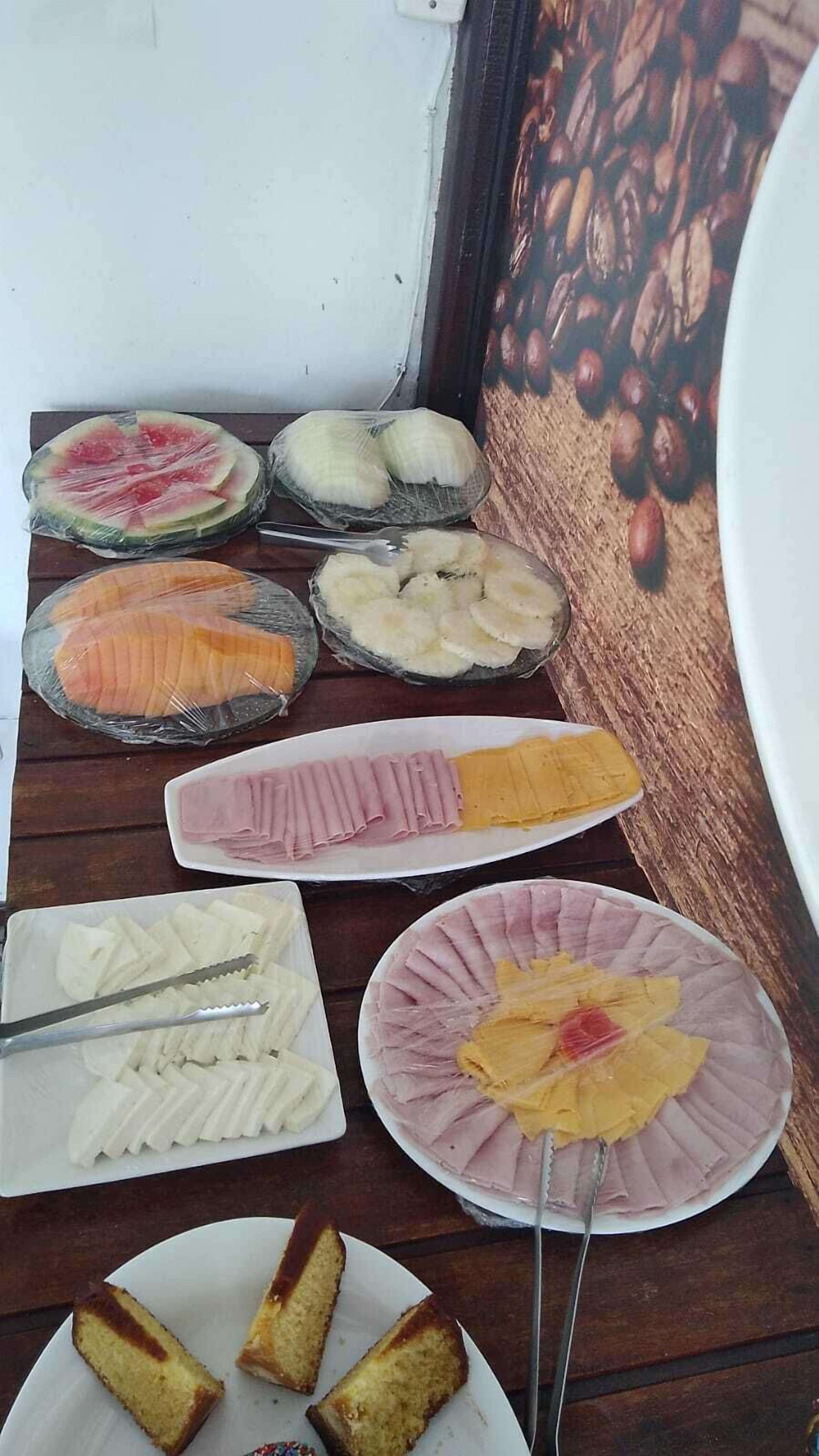 A variety of food items including watermelon slices, cheese, ham, and bread on a wooden table.