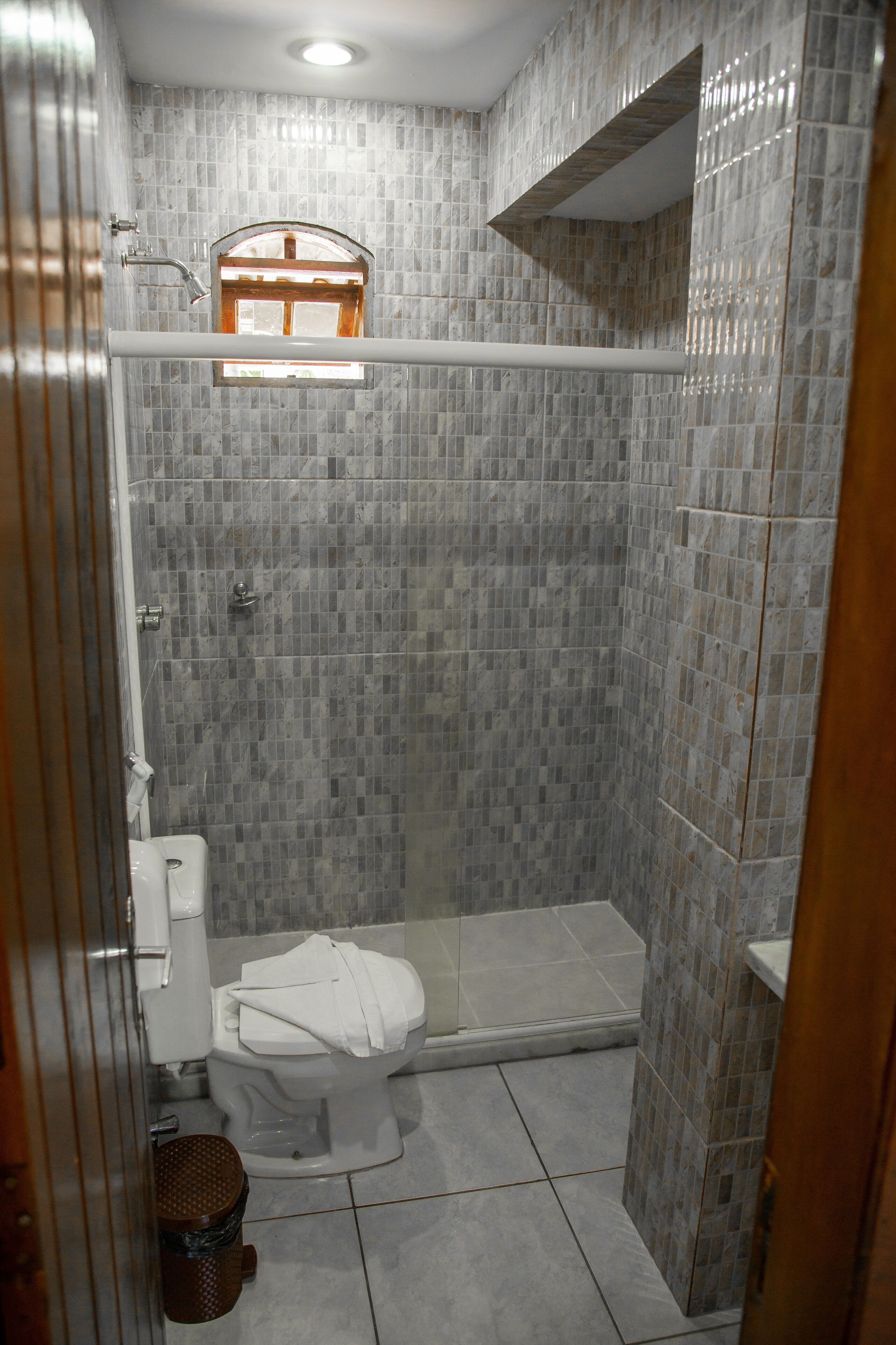 A bathroom with a shower, toilet, and a small window.